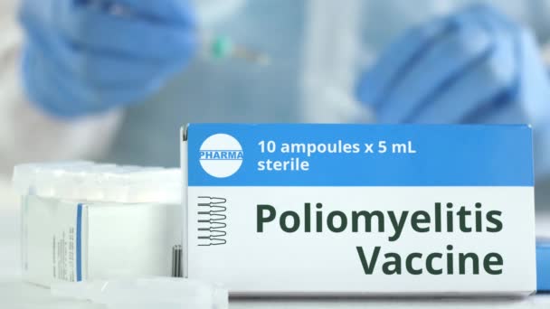 Kartong med polio vaccin på bordet mot suddig labb assistent eller läkare. Fiktiva läkemedlets logotyp — Stockvideo