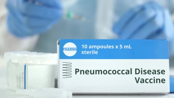 Kotak dengan vaksin penyakit pneumokokus di atas meja melawan asisten lab kabur. Logo phaceutical Fiksional — Stok Video