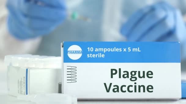 Ампулы с вакциной против чумы на столе рядом с работающим лаборантом, вымышленный логотип на коробке — стоковое видео