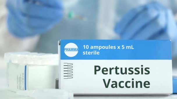 Коробка с вакциной против коклюша на столе против размытого лаборанта или доктора. Вымышленный фармацевтический логотип — стоковое видео