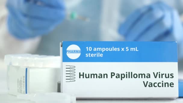 Box with human papilloma virus HPV vaccine on the table against blurred lab assistant or doctor. Fictional phaceutical logo — Stock Video