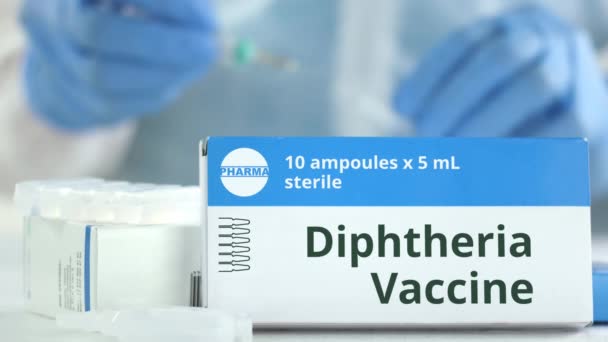 Doos met difterie vaccin op tafel tegen wazig lab assistent. Fictief phaceutisch logo — Stockvideo