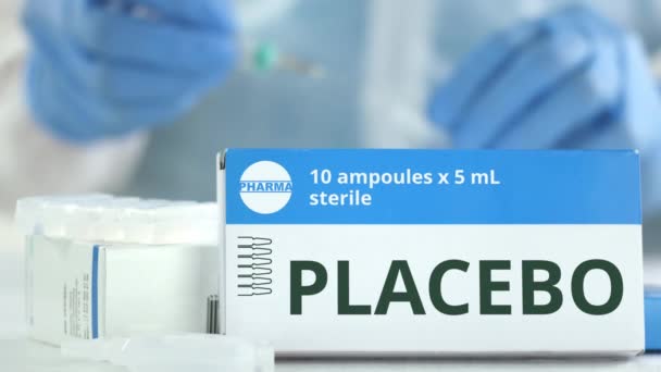 Box mit Placebo-Medizin auf dem Tisch gegen verschwommene Laborassistentin. Fiktives pharmazeutisches Logo — Stockvideo