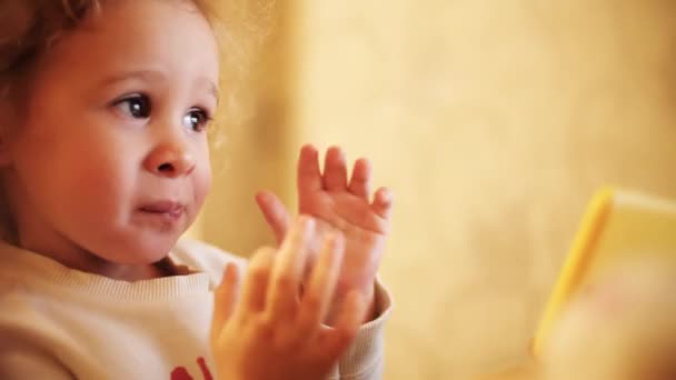 Grappig blond baby meisje glimlacht en apen tijdens het kijken naar cartoons op de smartphone — Stockvideo