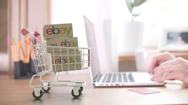 EBAY logó a dobozokon a bevásárlókosárban a laptop közelében. Szerkesztői online vásárlás otthonról 3D renderelés — Stock Fotó
