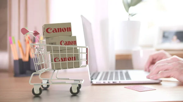 CANON logotyp på lådor i kundvagnen nära den bärbara datorn. Redaktionell online shopping hemifrån 3D-rendering — Stockfoto