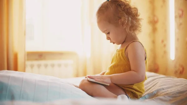 Focada menina olha para fotos no pequeno livro em quarto ensolarado em casa — Fotografia de Stock