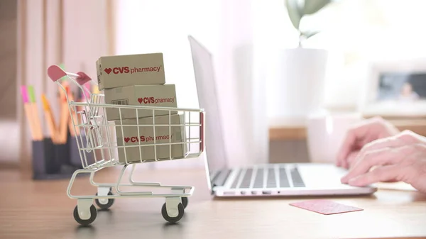 Dobozok CVS PHARMACY logóval a bevásárlókocsiban, a vásárló közelében laptoppal. Szerkesztői online vásárlás otthonról 3D renderelés — Stock Fotó