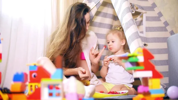 Jovem mulher grávida e sua filha comem bagas na tenda de brinquedo em casa — Fotografia de Stock