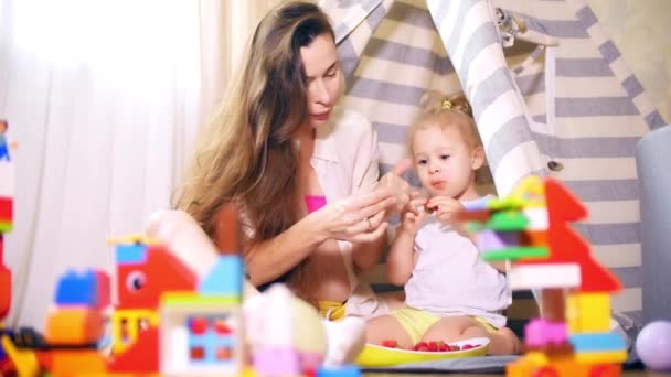 Молодая беременная женщина и ее дочь едят ягоды в игрушечной палатке на вигваме дома — стоковое видео