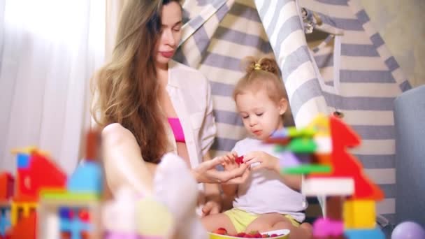 Красива вагітна жінка і її маленька дитина їдять малину в іграшковому наметі — стокове відео