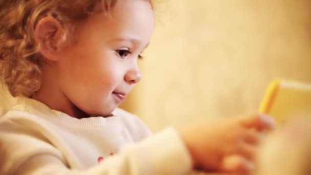 Krullend blond baby meisje maakt gebruik van moderne smartphone — Stockvideo