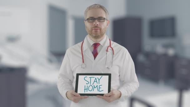 Заинтересованный врач держит планшетный компьютер с текстом "Остаться дома". Самоизоляция во время новой вспышки коронавируса COVID-19 — стоковое видео