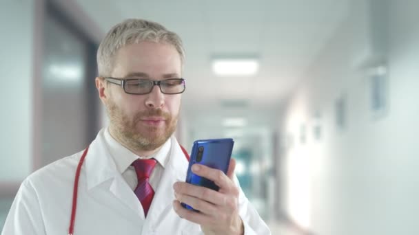 Dokter praat met een patiënt op zijn mobiele telefoon in een ziekenhuisgang — Stockvideo