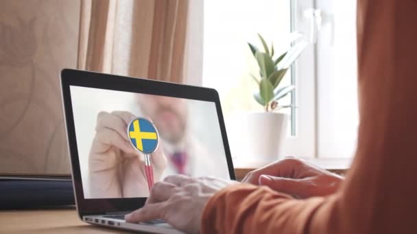 Ιατρικοί γιατροί βιντεοκλήση στο φορητό υπολογιστή στο σπίτι, στηθοσκόπιο καμπάνα με τη σουηδική σημαία. Τηλεϊατρική στη Σουηδία — Αρχείο Βίντεο