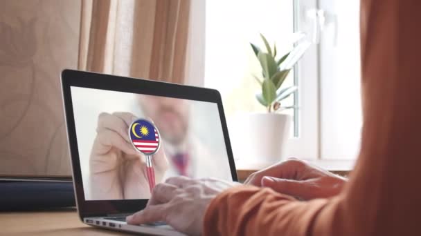 Doktor a számítógép képernyőjén és sztetoszkóp Malajzia zászlajával. Malajziai távorvoslás — Stock videók