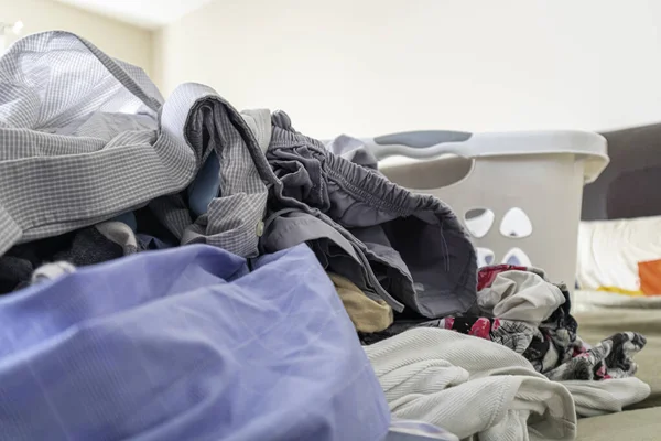 Куча свежевыстиранной одежды на кровати с корзиной для белья на заднем плане — стоковое фото