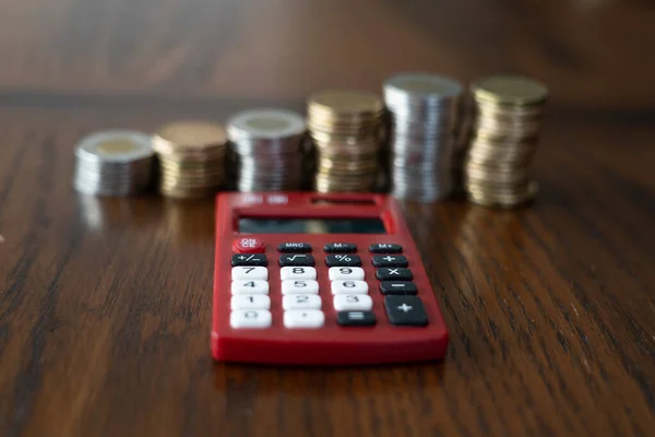 Piros zseb kalkulátor halom érmékkel a háttérben — Stock Fotó