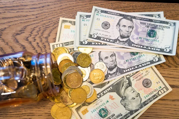 Bankbiljetten bedekt met munten die uit een glazen pot worden gegoten — Stockfoto