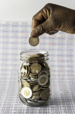Afrikalı Amerikalı Nijeryalı kadın RRSP kavanozuna bozuk para atıyor.