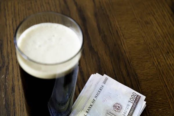 Egy pohár erős sör nigériai naira jegyekkel egy bárban. — Stock Fotó