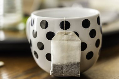 Dışarıda çay poşeti asılı, benekli çay fincanı.