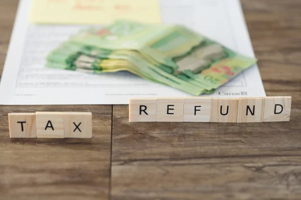 Reembolso de impuestos deletreado con fichas Carta con formulario de impuestos canadienses y dólares canadienses — Foto de Stock