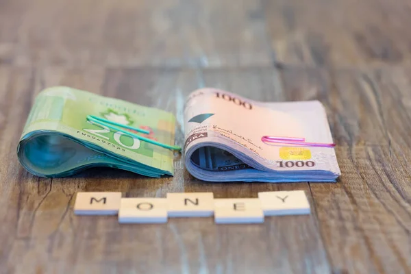 nigerian Naira and Canadian Dollar Bank notes with letter tiles spelling Money on table