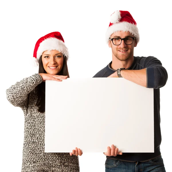 Young couple in santa hats holding blank board for advertisment. — Stock Photo, Image