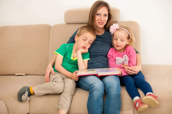 Mutter liest ihren Kindern auf Couch im Wohnzimmer ein Märchenbuch vor — Stockfoto
