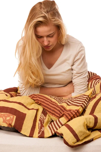 Woman sitting on bed holding belly because of the pain in stomac — Stock Photo, Image