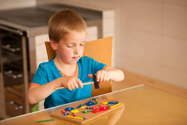 Chłopiec bawi się bloki i gwoździe na stole w kuchni — Zdjęcie stockowe