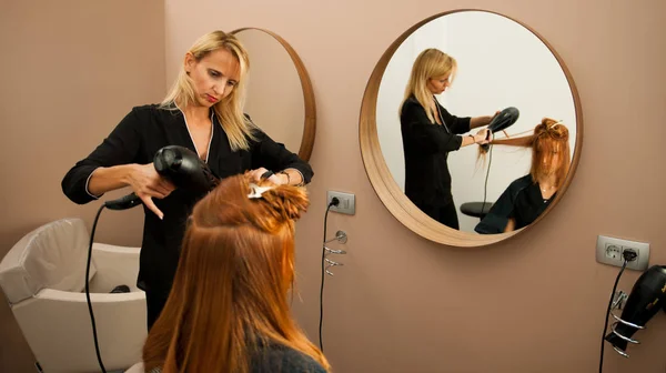 Стилист сушки волос клиентки в салоне красоты - хай — стоковое фото