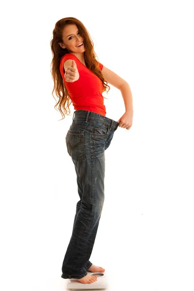 Beautiful young woman holding scale and too big trousers as she — Stock Photo, Image