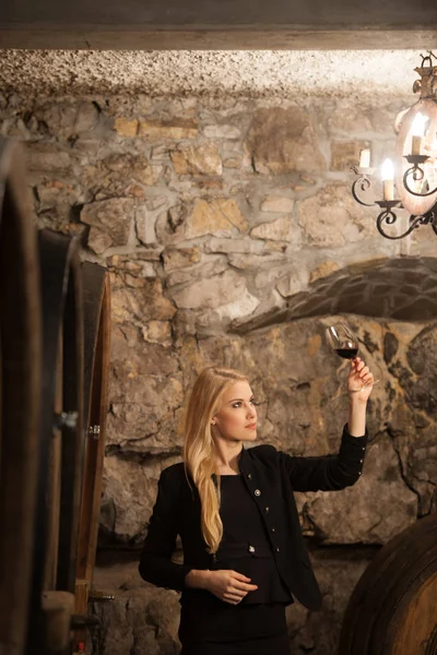 Mooie jonge blonde vrouw drinkt wijn in wijnkelder — Stockfoto