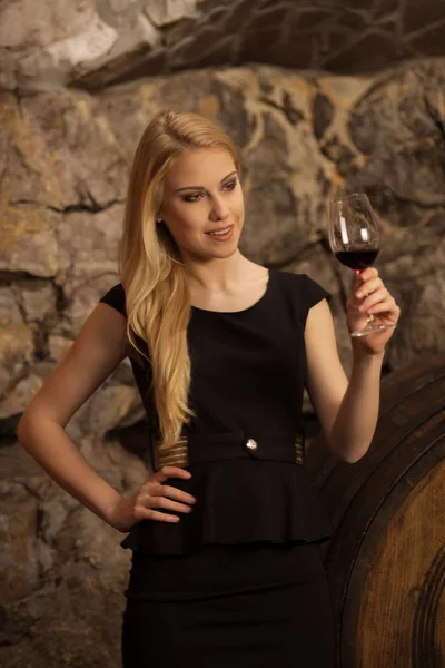 Beautiful young blond woman drinks wine in wine cellar — Stock Photo, Image