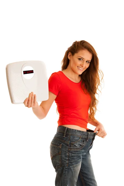 Beautiful young woman holding scale and too big trousers as she — Stock Photo, Image