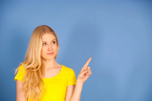 Schöne junge Frau in gelbem T-Shirt weist auf Kopierraum hin — Stockfoto