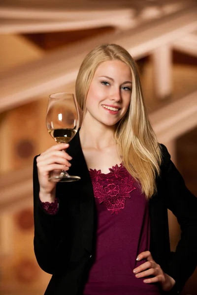 Beautiful young blond woman drinks wine in wine cellar — Stock Photo, Image