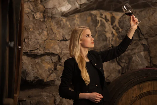 Beautiful young blond woman drinks wine in wine cellar — Stock Photo, Image