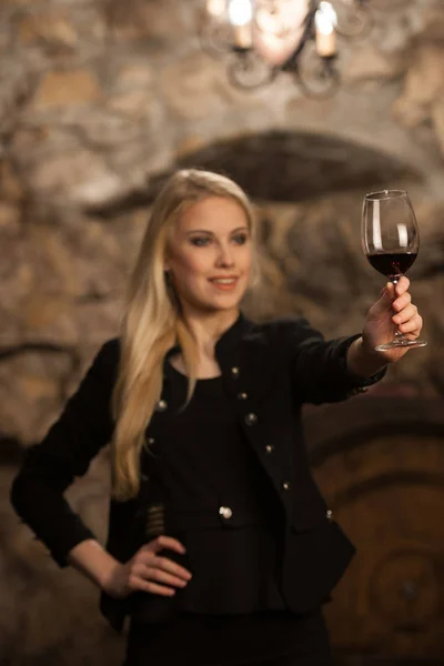 Beautiful young blond woman drinks wine in wine cellar — Stock Photo, Image