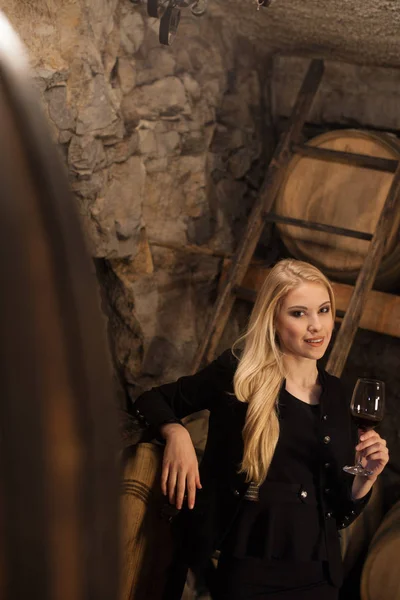 Beautiful young blond woman drinks wine in wine cellar — Stock Photo, Image