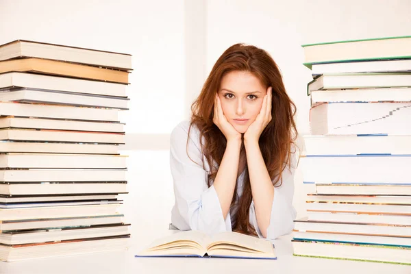 Attractive young woman studies wtih hugr book piles on her desk — Stock Photo, Image