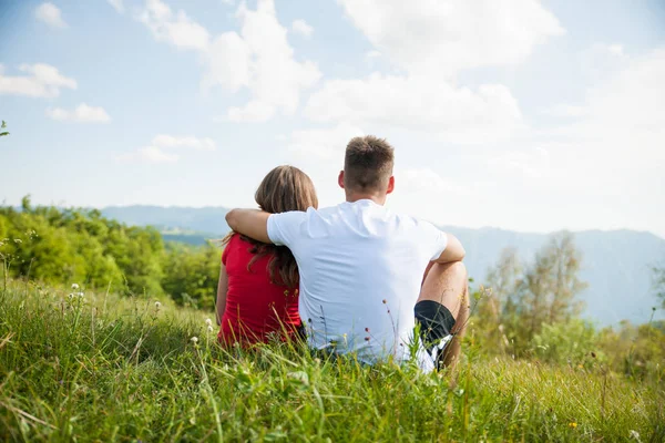 Pareja activa descansa en un pico de montaña mirando en un lan de montaña —  Fotos de Stock