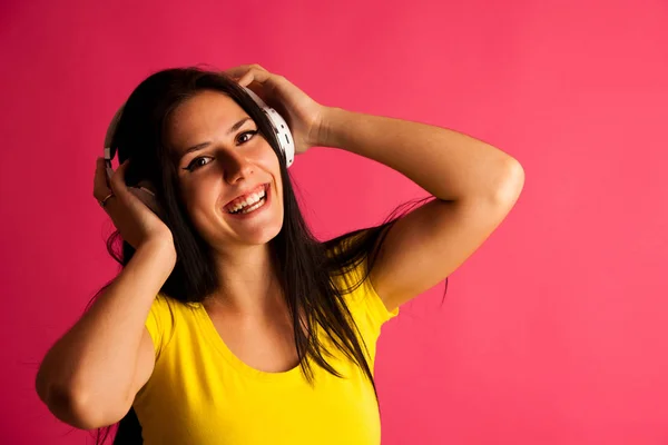 Attraente giovane donna ascolta musica su sfondo rosa — Foto Stock