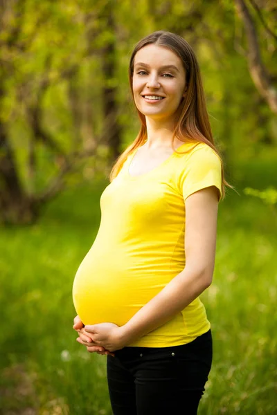Schwangere Frau im gelben T-Shirt auf einer grünen Wiese im Frühling — Stockfoto