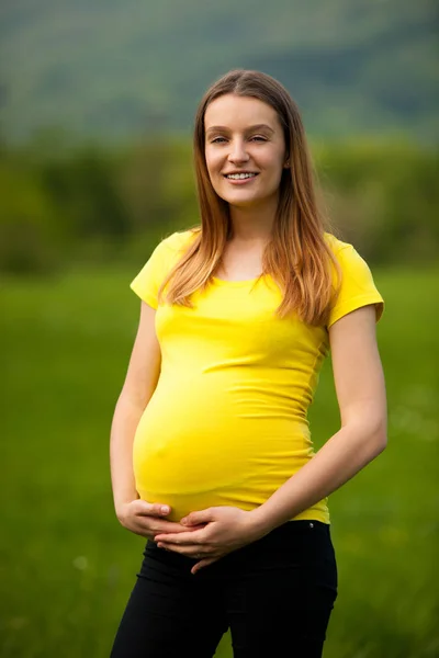 Schwangere Frau im gelben T-Shirt auf einer grünen Wiese im Frühling — Stockfoto