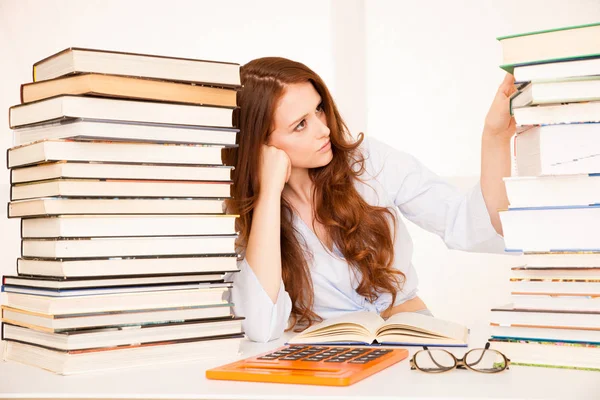 Attractive young woman studies wtih hugr book piles on her desk — Stock Photo, Image