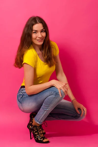 Atractiva joven en jeans y camiseta amarilla sobre bac rosa —  Fotos de Stock