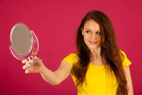 年轻漂亮的女人看自己镜子里在充满活力的粉红色 — 图库照片